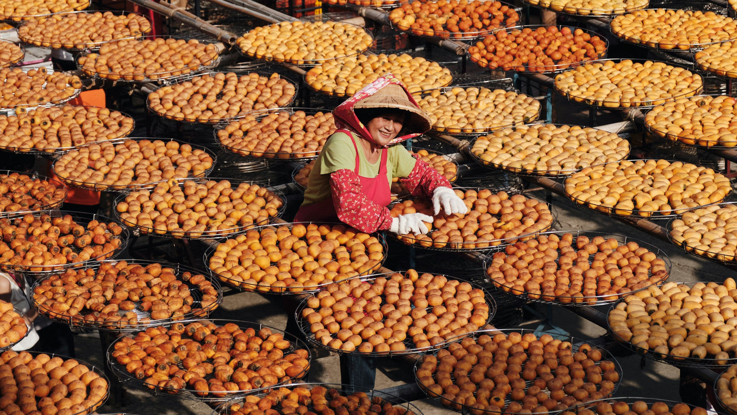 Woman arranging fruits on a large outdoor setup with a red building in the background.